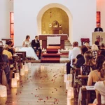 Braut und Bräutigam sitzend während Trauung in Kirche bei Altar, mit Kirchgang und Gästen, Pfarrer spricht auf Kanzel, Deko, indoor