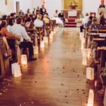 Braut und Bräutigam sitzend während Trauung in Kirche mit Kirchgang und Gästen Deko indoor