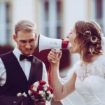 Paarshooting, Braut schreit Bräutigam durch Megafon an Hochzeitsstrauß Brustbild outdoor