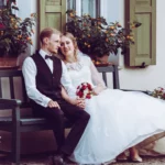 Paarshooting, Braut und Bräutigam Hochzeitsstrauß sitzend auf Bank Ganzkörper outdoor