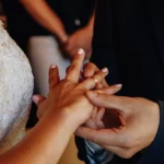 Bräutigam steckt Braut Ring an Ausschnitt Hände indoor