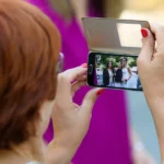 Ausschnitt, Brautmutter fotografiert Braut mit Freundinnen mit Handy, outdoor